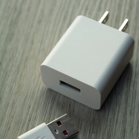 Carregador de parede USB branco com cabo, sobre mesa de madeira